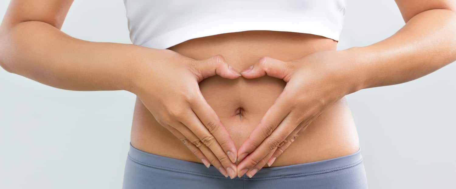 A woman making a heart with her hands over her stomach after a tummy tuck to fix diastasis recti