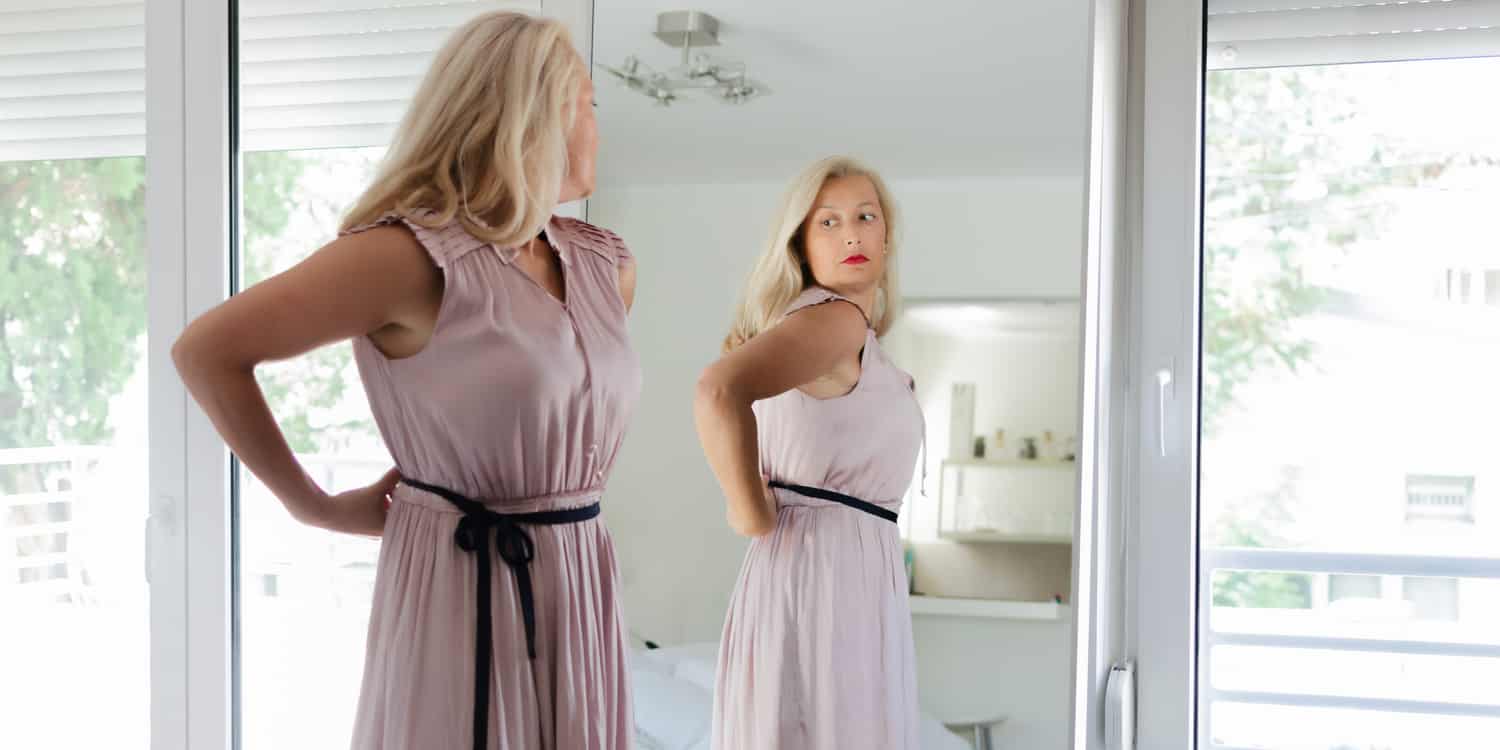 A woman looking in the mirror, representing the link between plastic surgery and body image